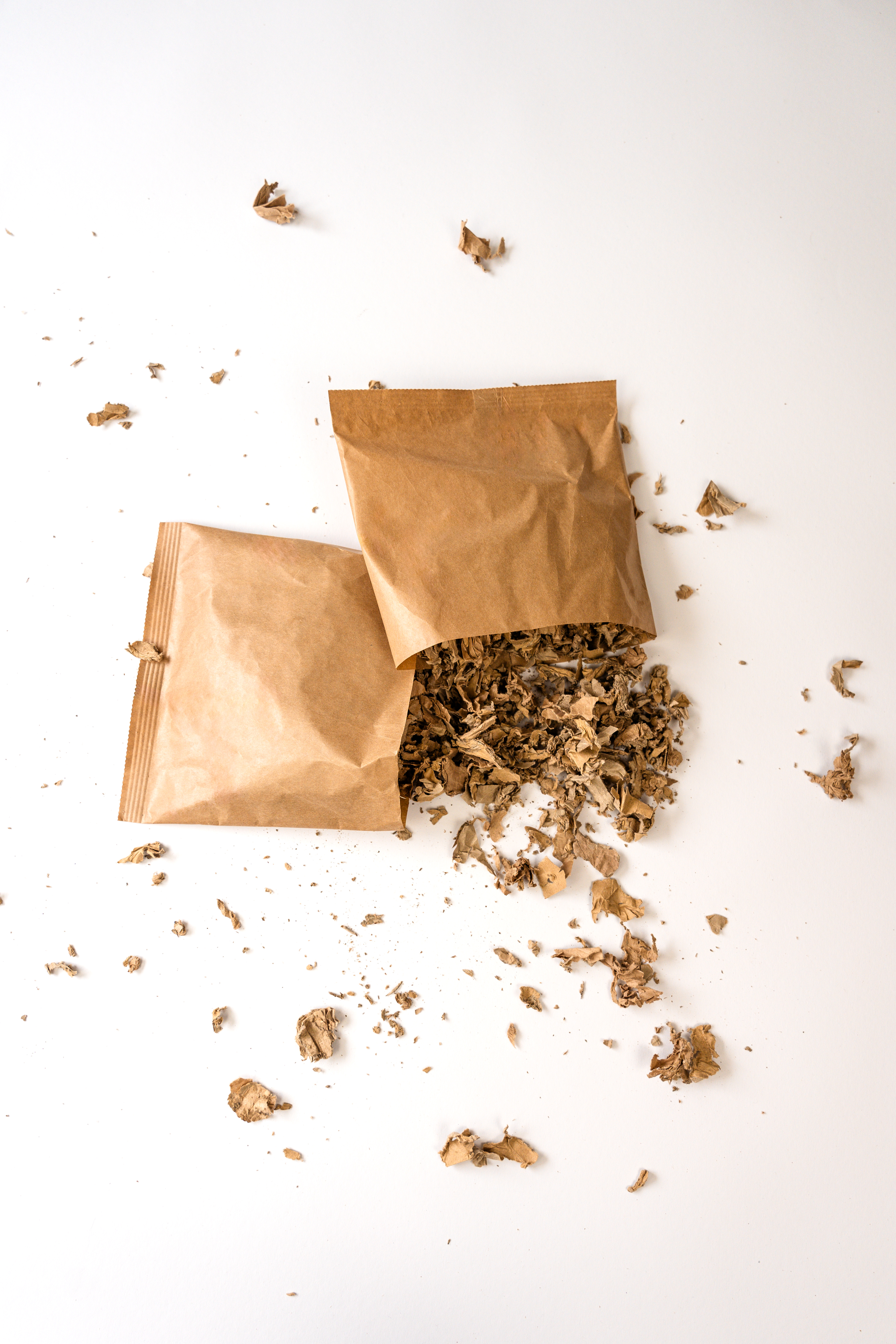 Ansicht von oben auf zwei nebeneinander liegende Füllkissen aus braunem Papier. Das linke Füllkissen ist unten aufgerissen. Vor dem Kissen liegen unter der Öffnung ganz viele braune Schnipsel aus Papier