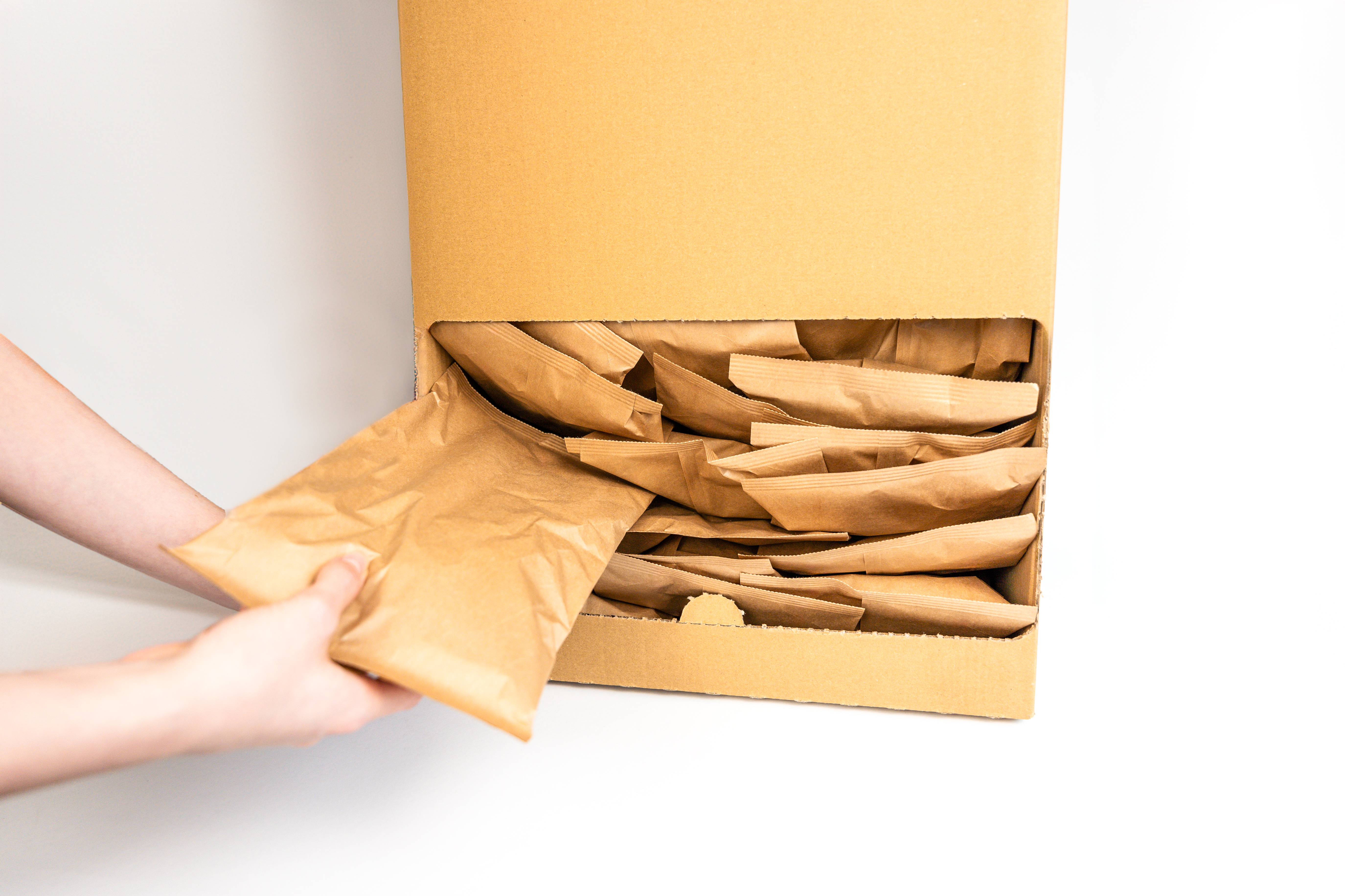 Ansicht von oben auf einen geöffneten Karton. Zwei Hände ziehen gerade ein Füllkissen aus braunen Papier aus dem Karton. Der Karton ist mit vielen weiteren Füllkissen aus Papier gefüllt